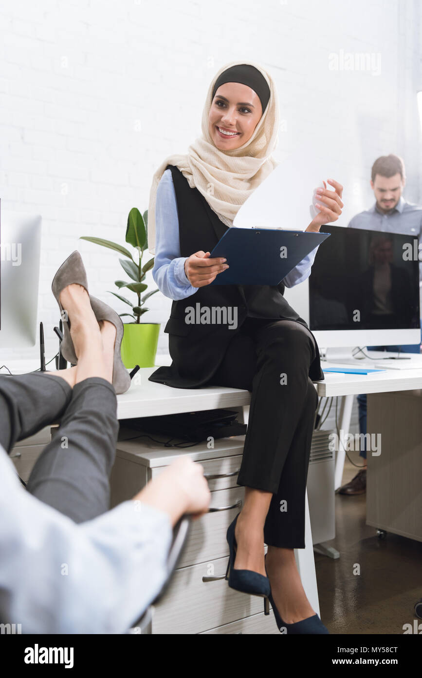 Selektiver Fokus der lächelnden arabisch Geschäftsfrau im hijab mit Notizblock in der Hand sitzen am Tisch im Büro Stockfoto