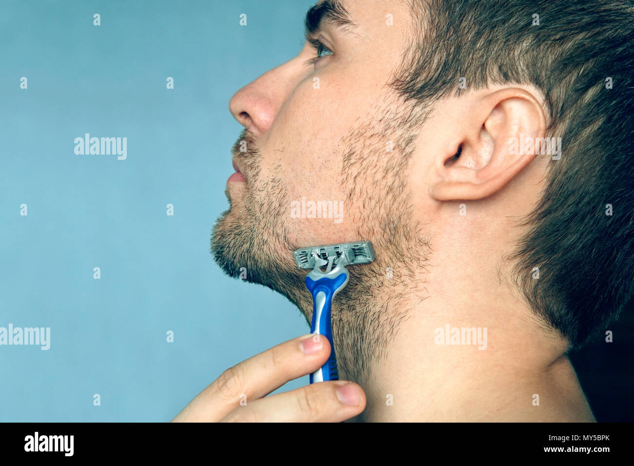 Ein Mann rasiert eine Rasur ohne Schaum, Seife und Creme. Rasieren Sie trocken. Plakat, mit kopieren. Copyspace Platz für Text. Stockfoto