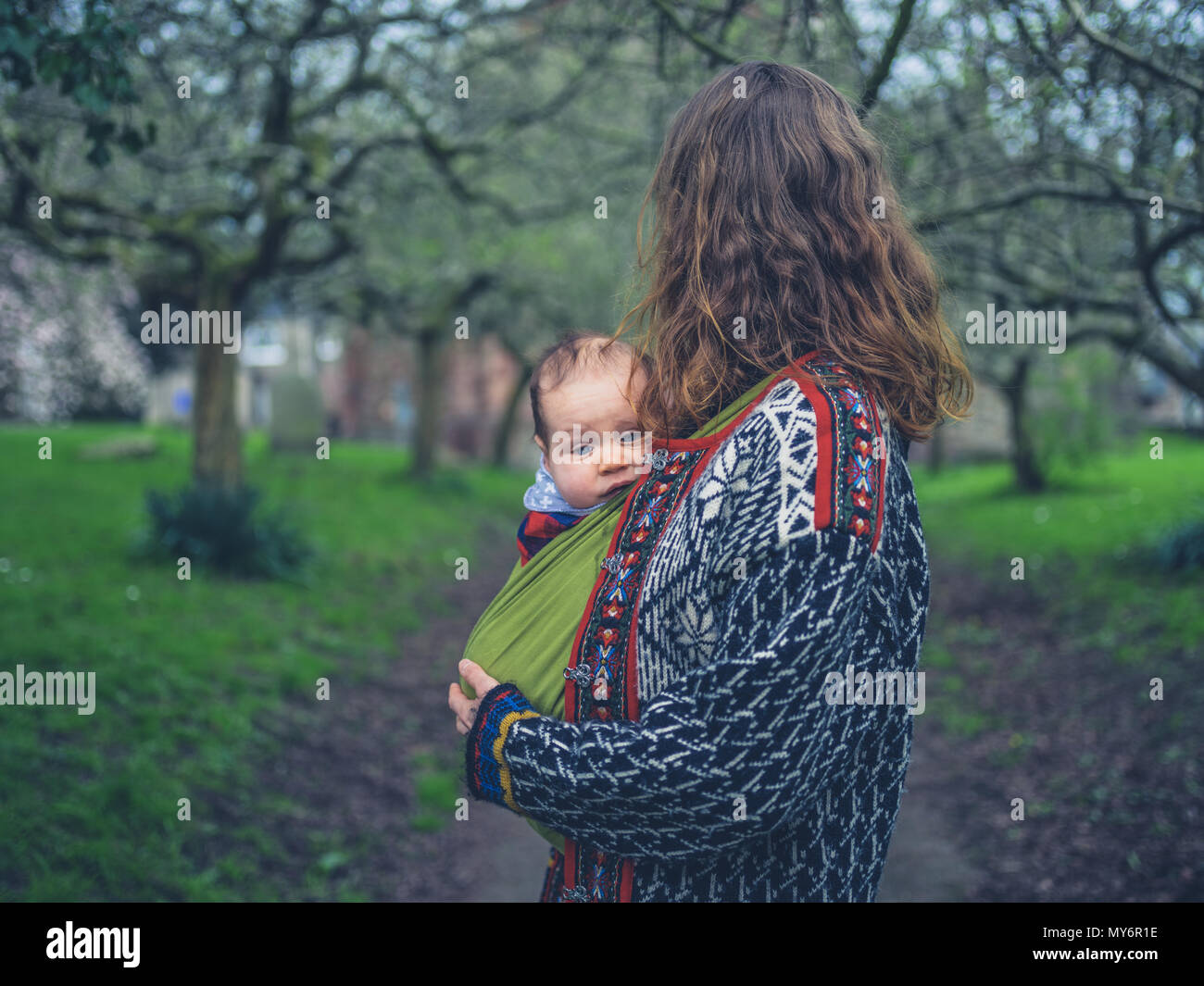 Eine junge Mutter steht im Park, mit ihrem Baby in einem Träger Schlinge Stockfoto