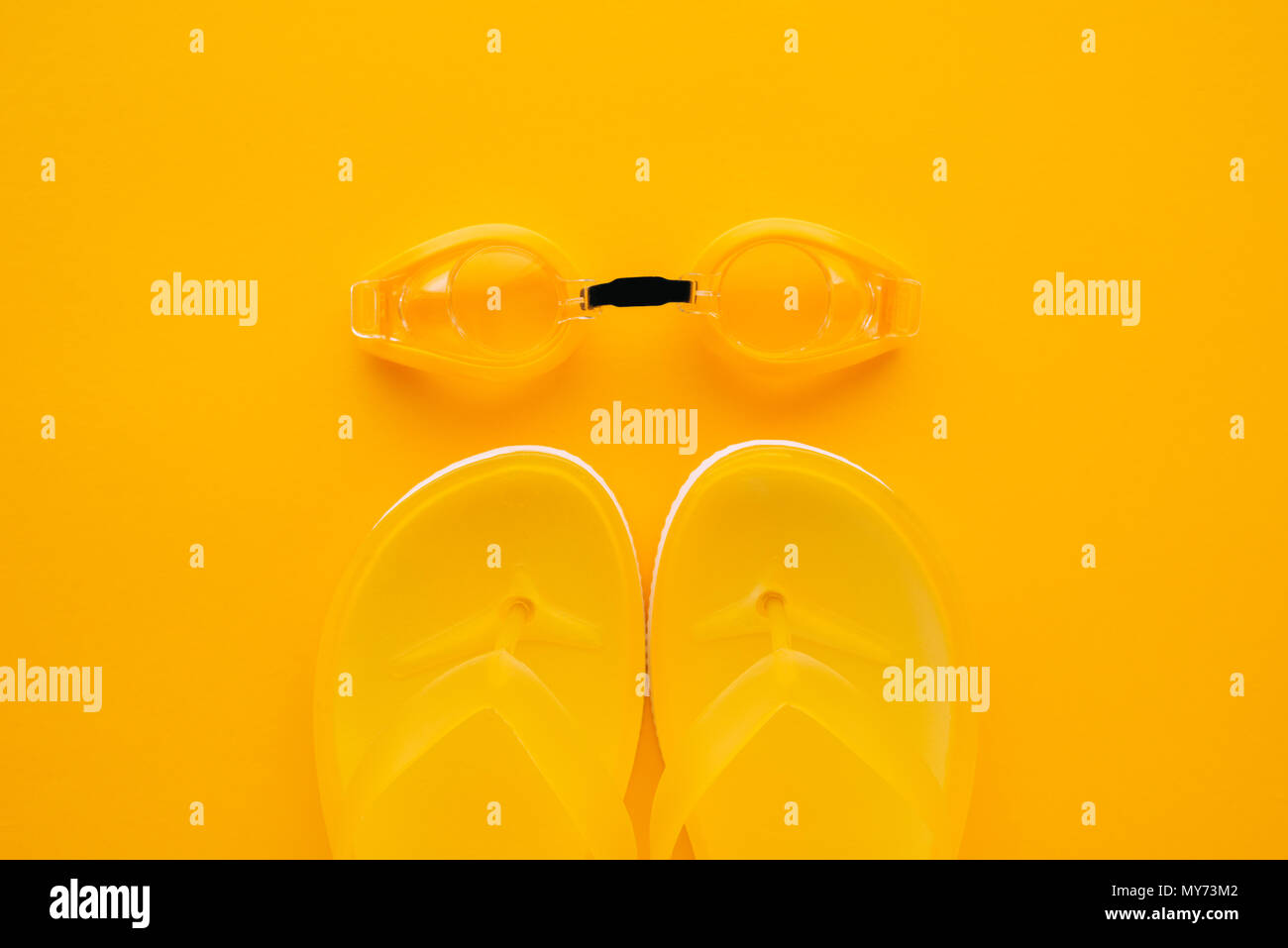 Schwimmbrille und Flip Flops auf gelbem Hintergrund, Ansicht von oben flach minimale Zusammensetzung Stockfoto