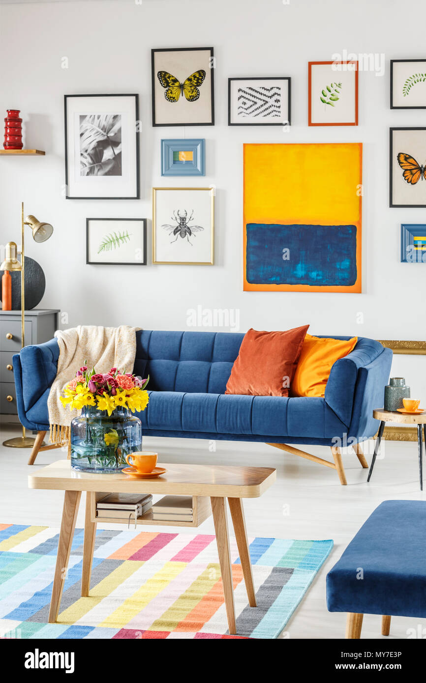 Strauß, frisch, Blumen in einer Glasvase auf einen hölzernen Tisch in der Mitte von einem hellen Wohnzimmer Innenraum mit blauen Sofa und Plakate an Stockfoto