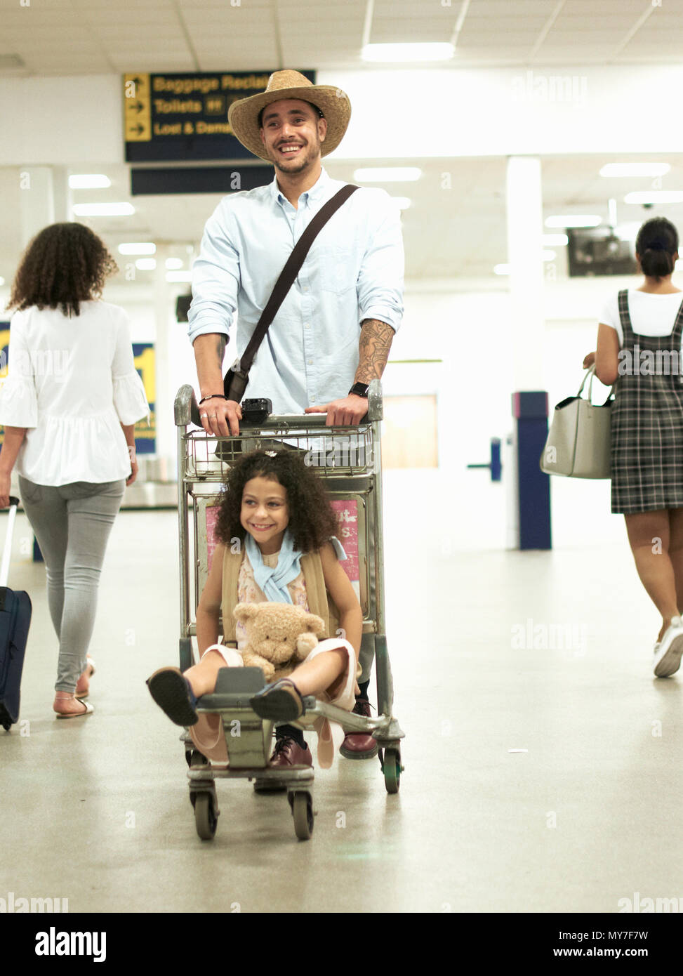 Vater mit Mädchen auf Gepäckwagen in Flughafen Stockfoto