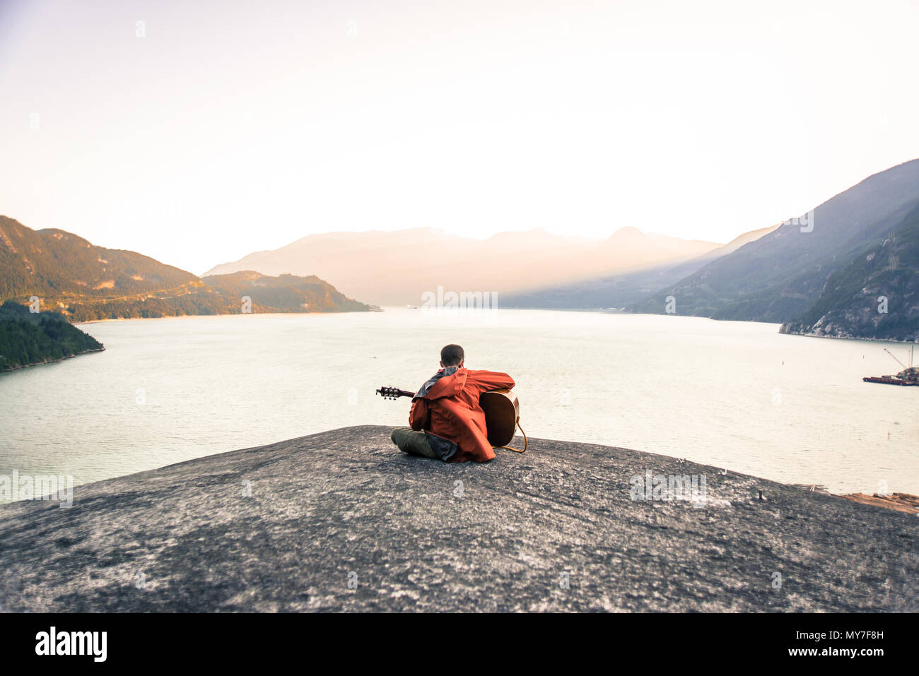 Junge Mann sitzt auf Der Malamute, Gitarre spielen, Rückansicht, Squamish, Kanada Stockfoto
