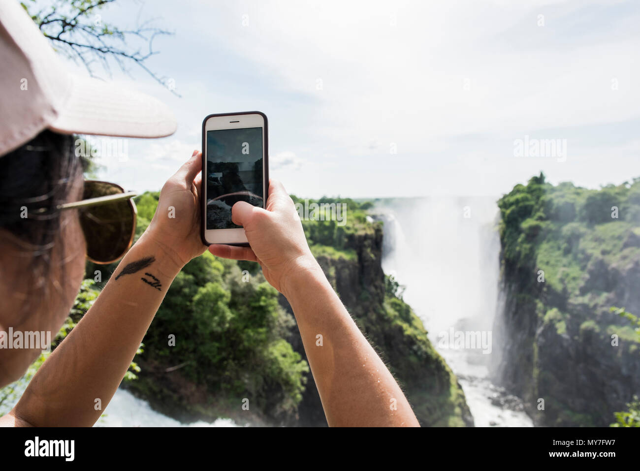Junge weibliche Tourist, Smartphone Fotos von Victoria Falls, Blick über die Schulter, Simbabwe, Afrika Stockfoto