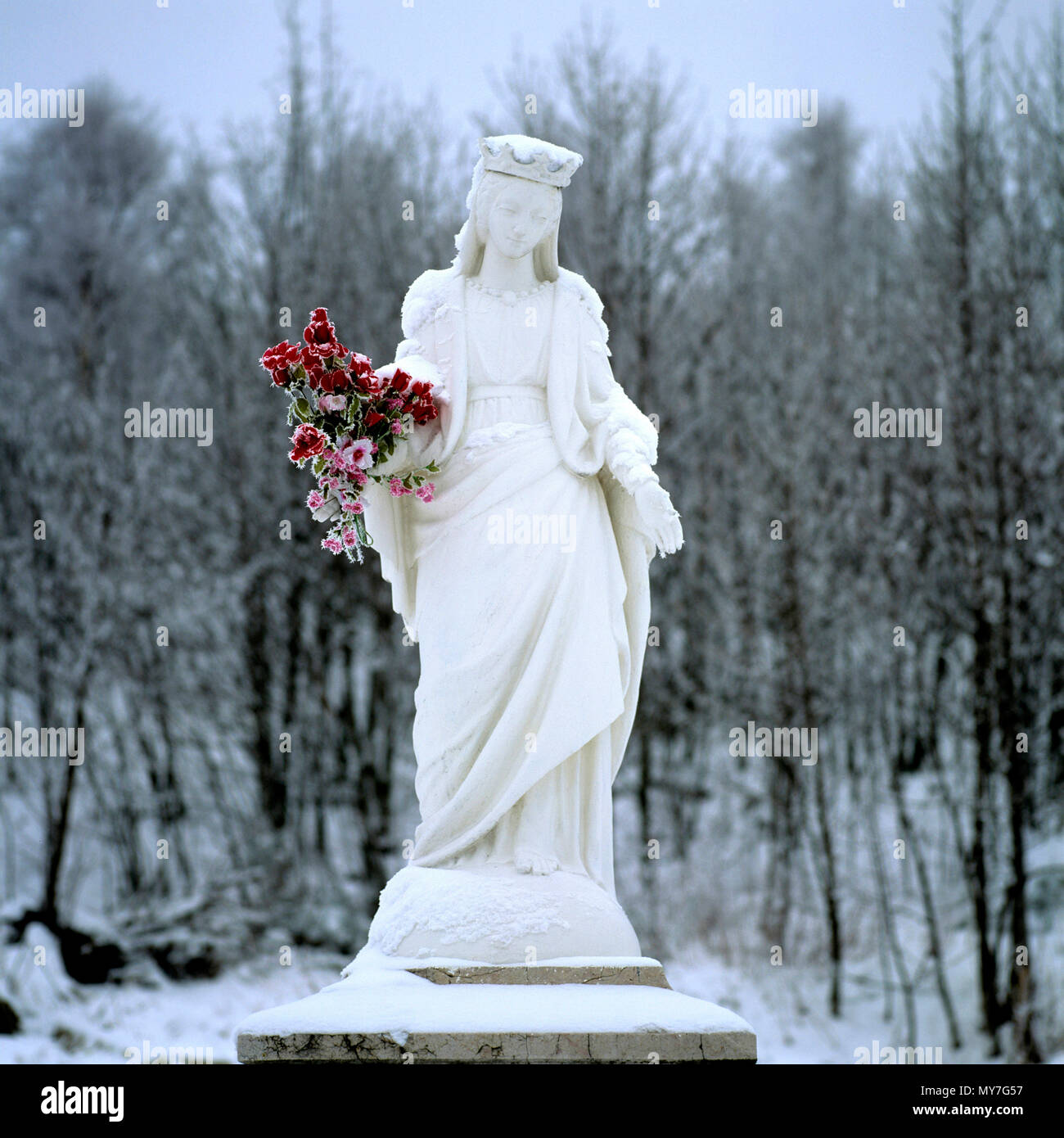 Weiße Statue einer Frau mit Blumen umgeben von Schnee in einer Winterlandschaft mit Bäumen im Hintergrund, Frankreich Stockfoto