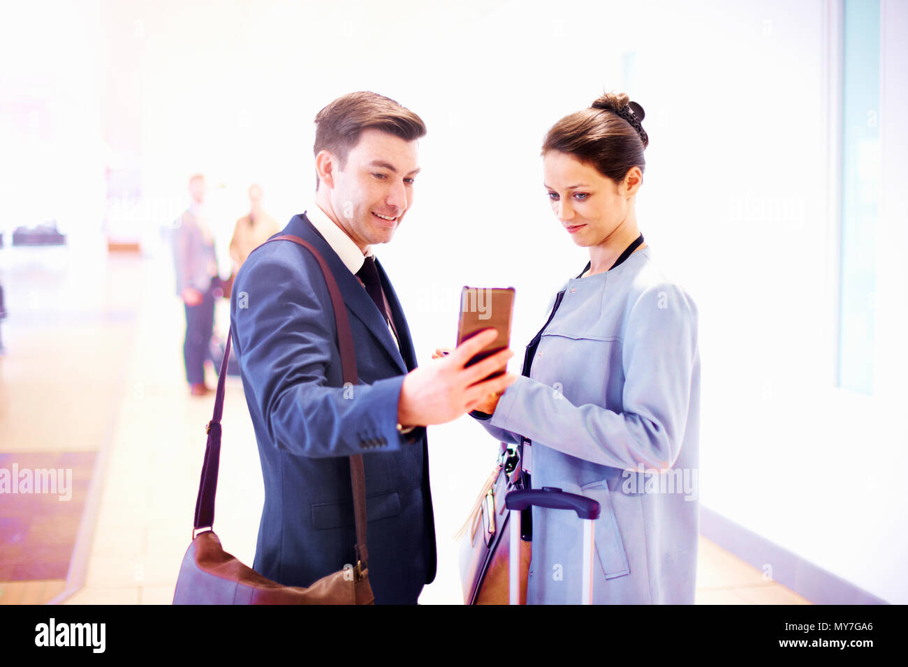 Junge Geschäftsfrau und Mann im Flughafen am Smartphone suchen Stockfoto