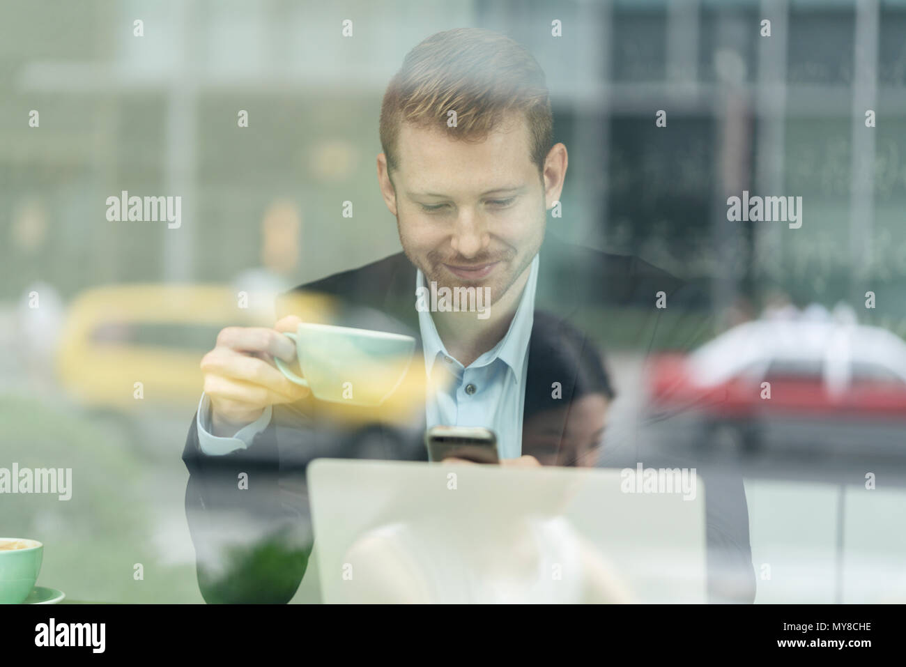 Unternehmer im Cafe sitzen, Kaffee trinken, mit Smartphone, durch das Fenster gesehen Stockfoto