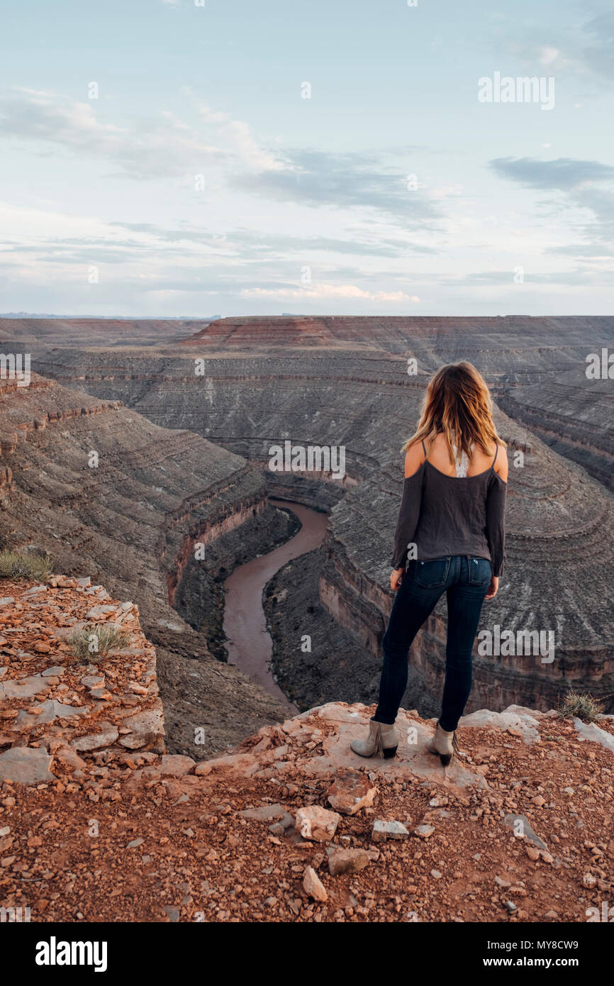 Junge Frau in remote Einstellung, stehend auf Klippe, an der Aussicht suchen, Rückansicht, Mexican Hat, Utah, USA Stockfoto