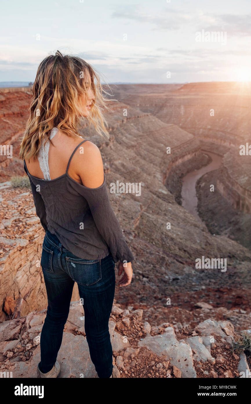 Junge Frau in remote Einstellung, stehend auf Klippe, an der Aussicht suchen, Rückansicht, Mexican Hat, Utah, USA Stockfoto