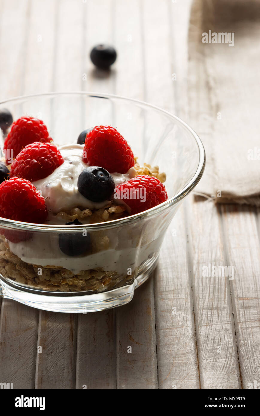 Himbeeren, Heidelbeeren, Müsli und Joghurt im Glas Schüssel auf Holzlatten. Gesundes Frühstück für ein gesundes Leben. Bild vertikal. Stockfoto