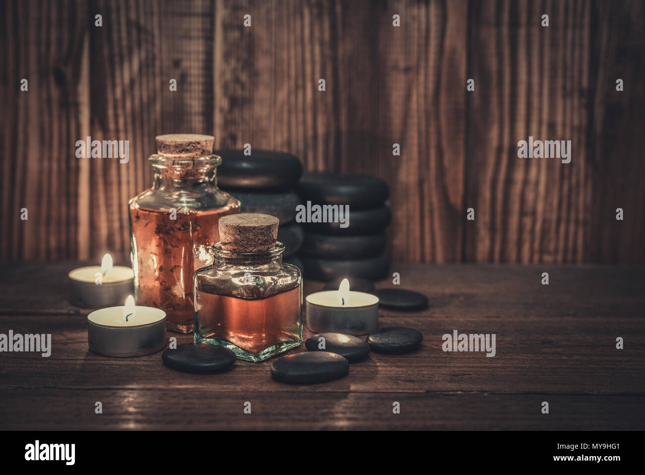 Massage Öl in vintage Flasche, Kerzen und Stein für Stein Massage auf Holz- Hintergrund Stockfoto