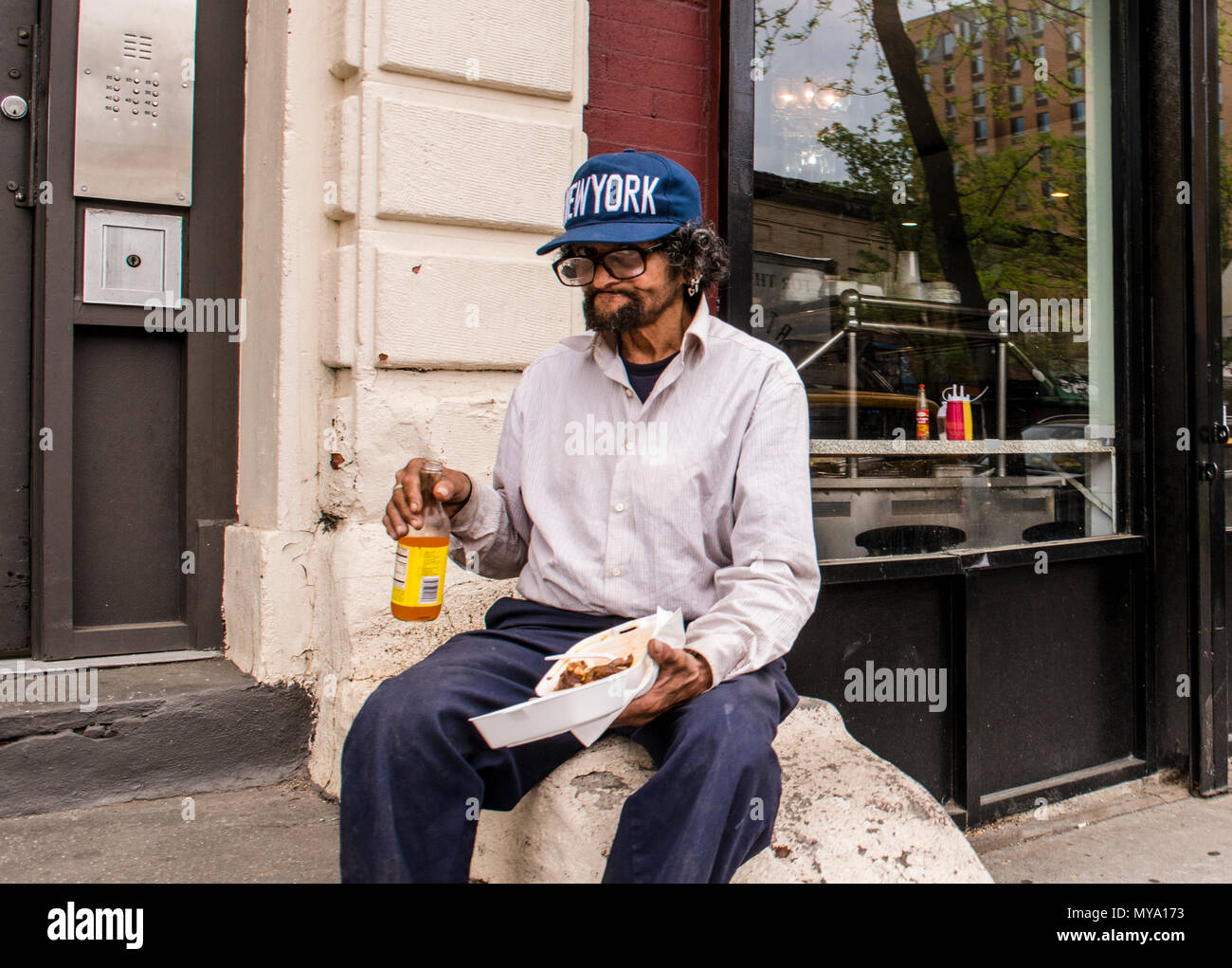 Porträt eines Mannes mit einer New York cap, sitzend an der Wand, das Mittagessen, der gerade in die Kamera Stockfoto