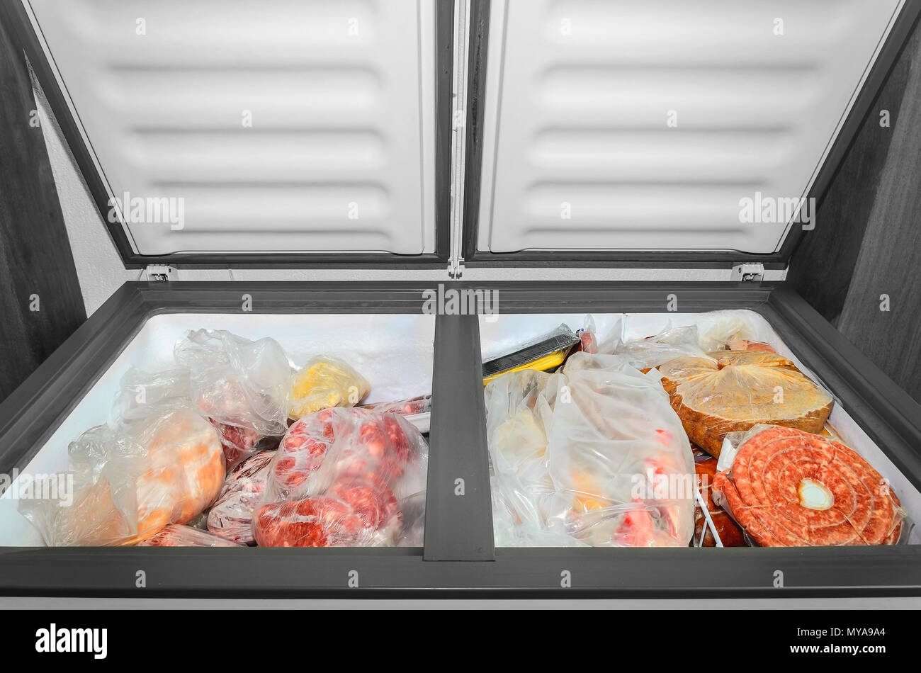 Gefrorene Lebensmittel im Gefrierschrank. Gefrorenes Fleisch und andere Lebensmittel, die in einem horizontalen Gefrierschrank Tüten mit den zwei Türen öffnen. Die Konservierung von Lebensmitteln. Stockfoto