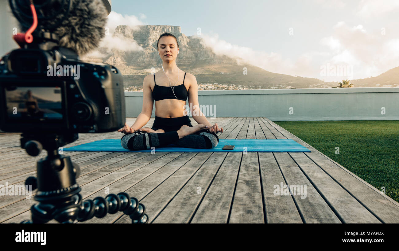 Blogger Aufnahme Inhalt zu Yoga und Meditation für Ihren Blog auf Kamera auf der Terrasse Ihres Hauses sitzend mit malerischem Hintergrund. Kamera montiert Stockfoto