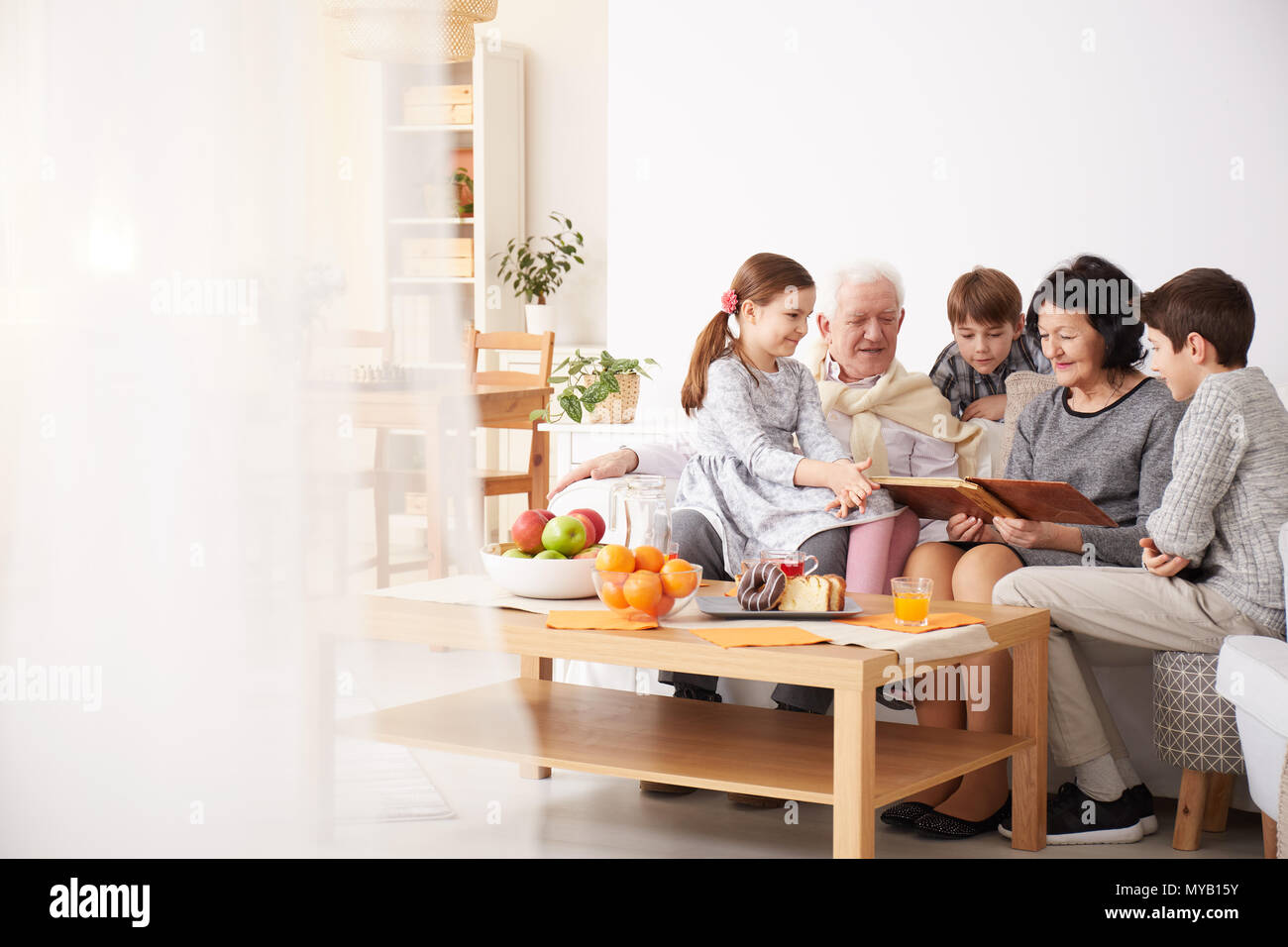 Glückliche Großeltern, Fotoalbum, um ihre Enkelkinder in einem Wohnzimmer Stockfoto