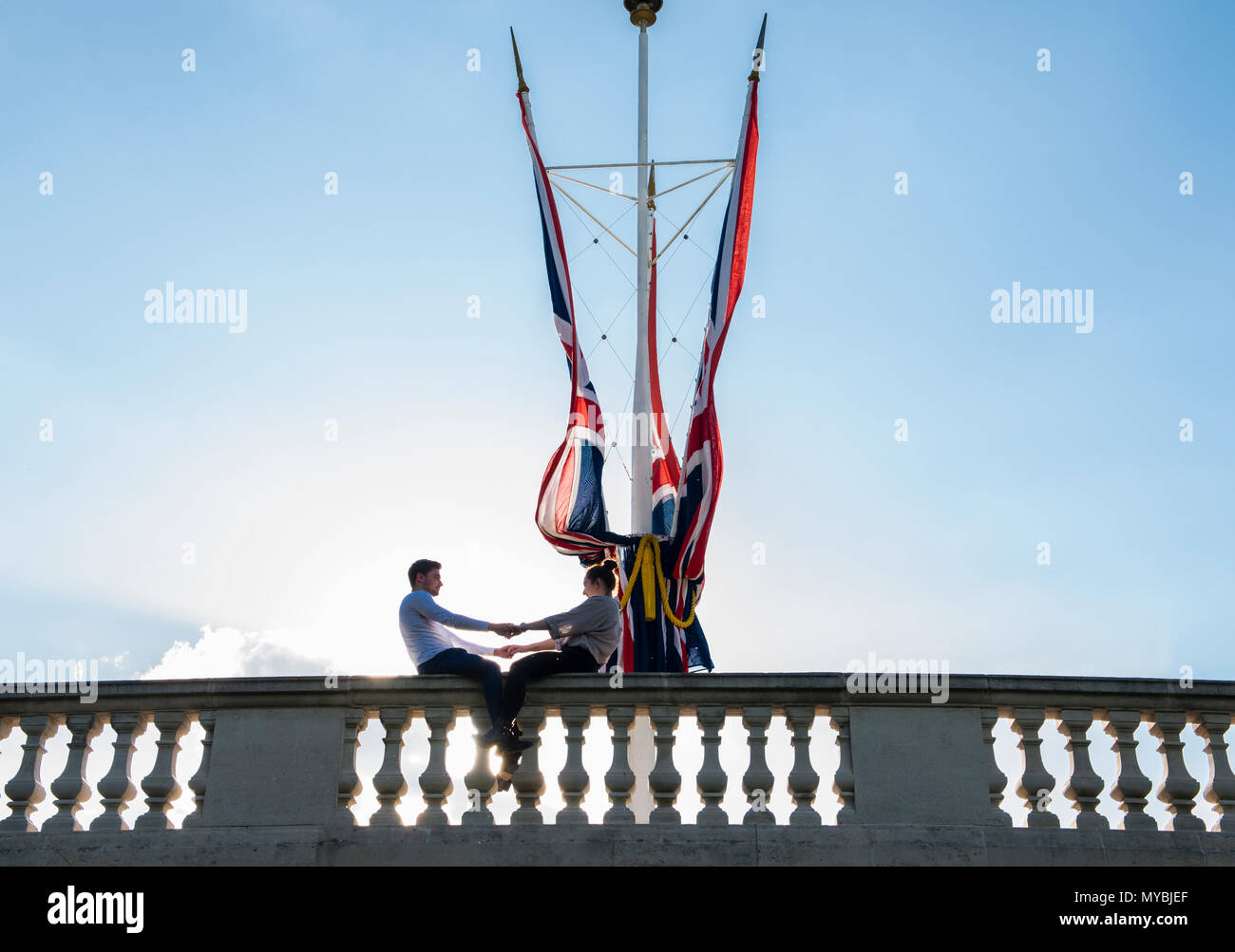 Junges Paar sitzt auf Wand, Hände halten, neben britischen Flaggen in St James's Park, London, England, Großbritannien Stockfoto