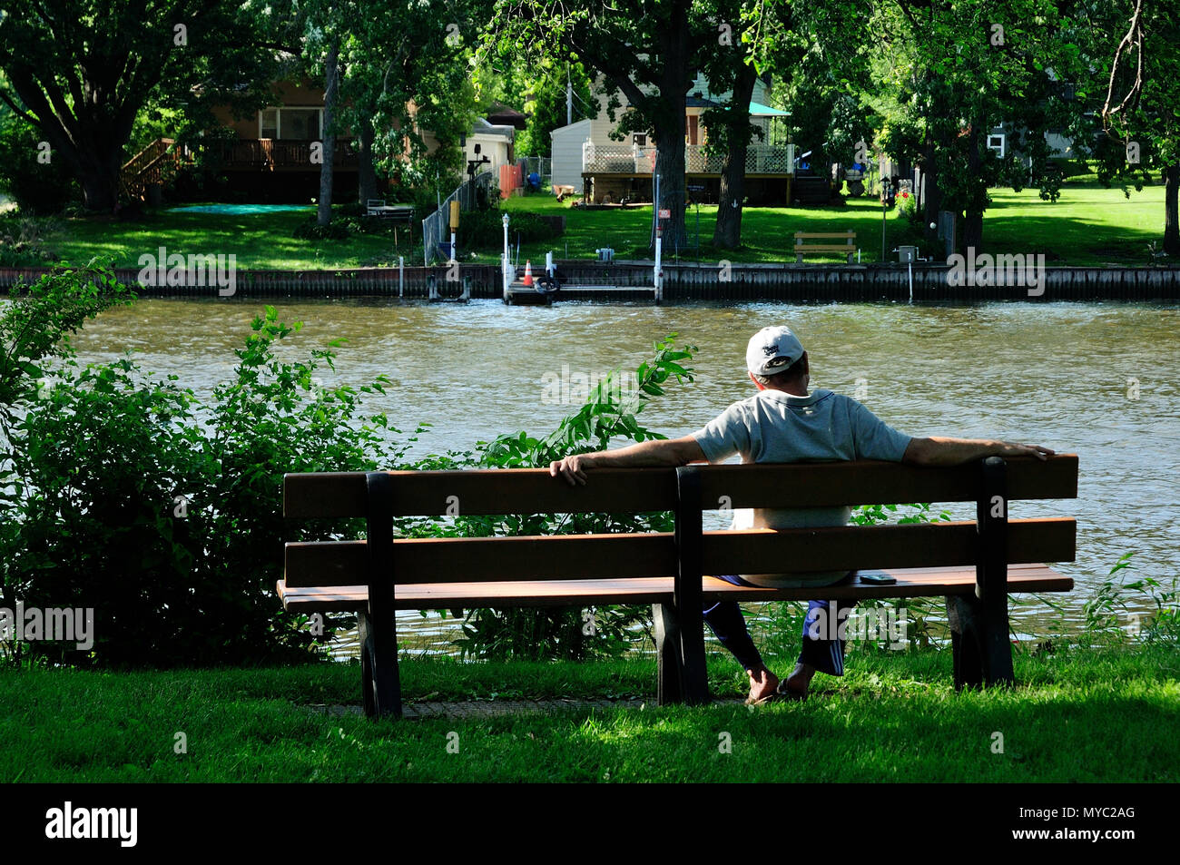 Mann sitzt auf einer Parkbank im Ruhestand am Fluss. Stockfoto