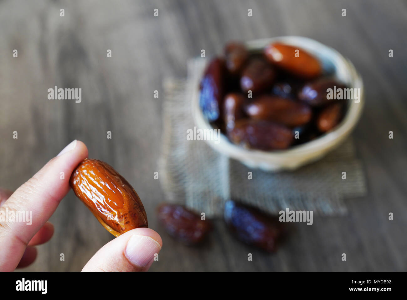 Menschliche finger Holding einzelnes Datum Obst und unscharfer Daten gefüllte Schüssel im Hintergrund Stockfoto