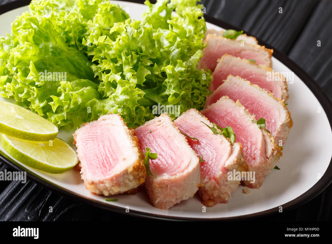 Ahi Thunfisch paniert serviert mit Salat und Kalk in der Nähe auf einer Platte auf einem Schwarzen Tisch. Horizontale Stockfoto