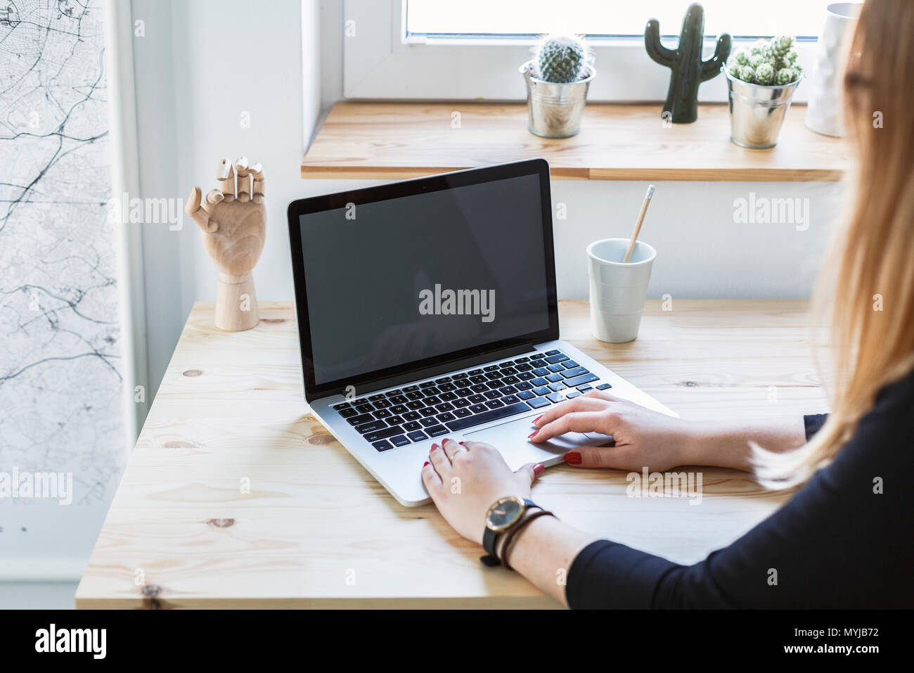 Frau Tippen auf Laptop mit Mockup vom Schreibtisch aus Holz im Home Office Interior Stockfoto