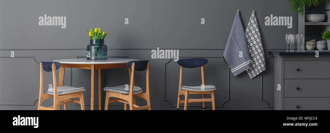 Grau, hölzerne Stühle am runden Tisch gegen graue Wand mit Spritzguss im Speisesaal Innenraum Stockfoto