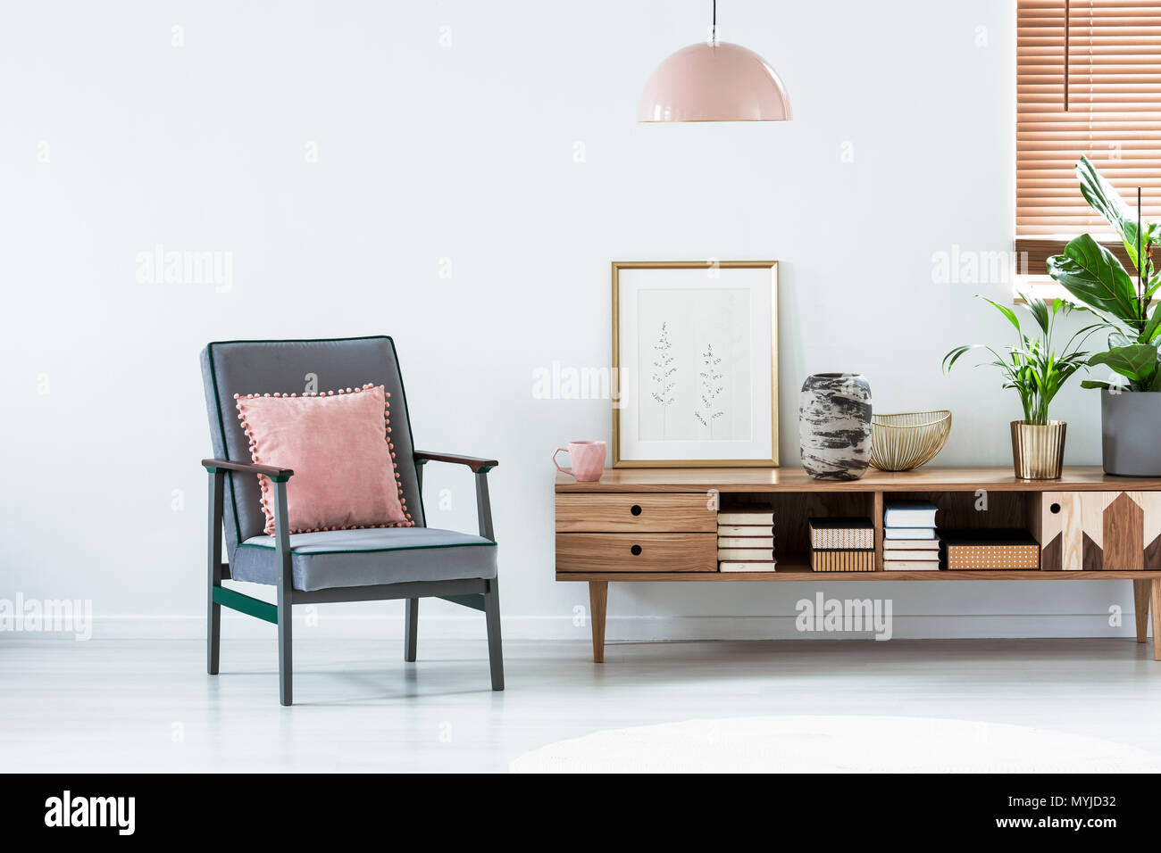 Pastellfarben Sessel neben einem Holzschrank mit Poster und Pflanze im Wohnzimmer Innenraum Stockfoto