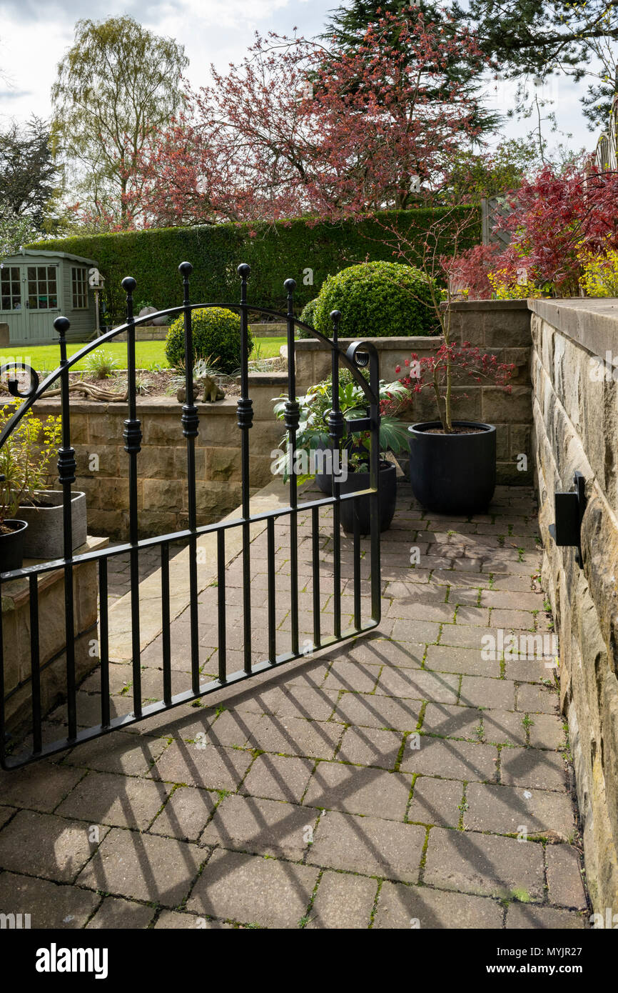 Blick durch das geöffnete Tor zu schönen, gepflegten, privaten Garten mit zeitgenössischem Design, Sträucher, Kugeln, Pfad & gepflegten Rasen - Yorkshire, England, Großbritannien Stockfoto