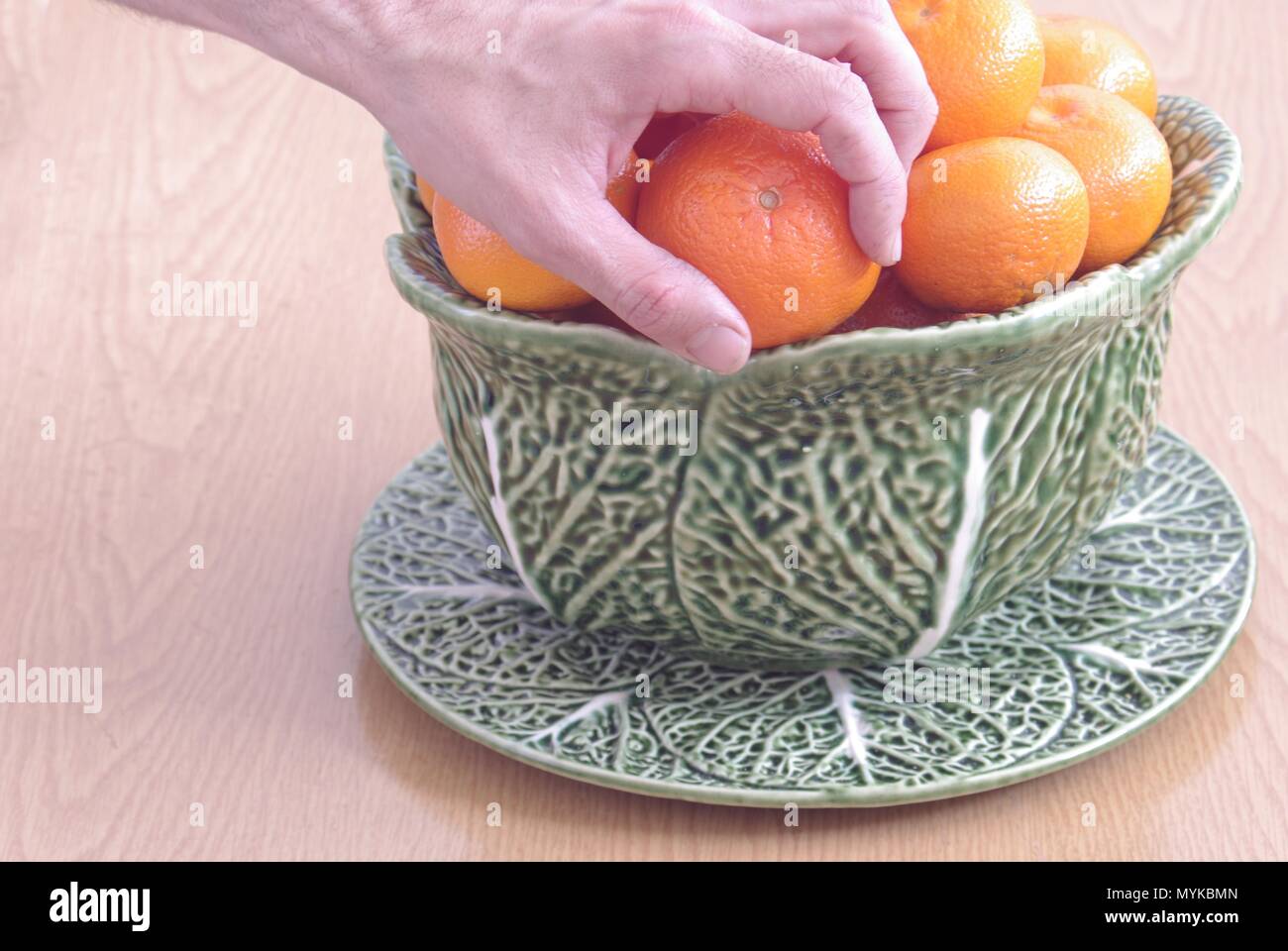 Eine Hand, die ein Mandarin eines fruiterer der Keramik auf einem Tisch aus Holz Stockfoto