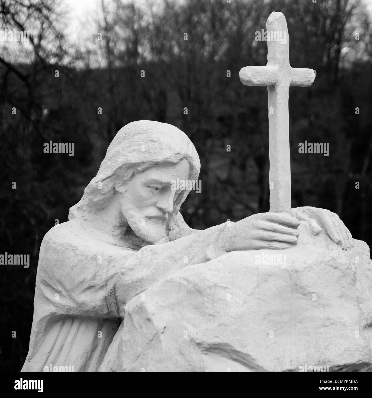 Weiß lackiert alte Statue Jesu Christi durch das Kreuz zu beten. Monochromes Bild Stockfoto