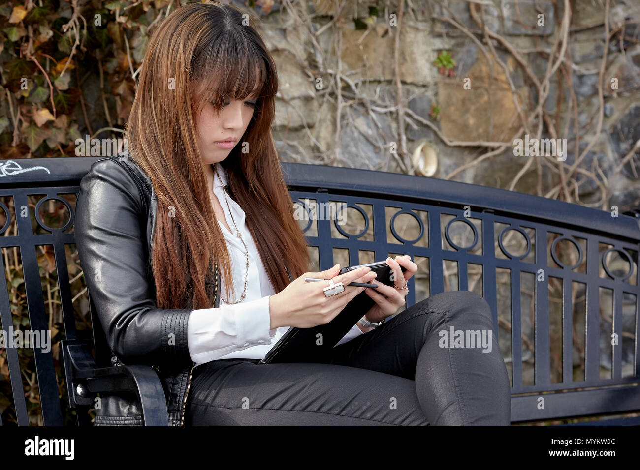 Asiatische Frau sitzt auf der Bank mit einem Tablet Stockfoto