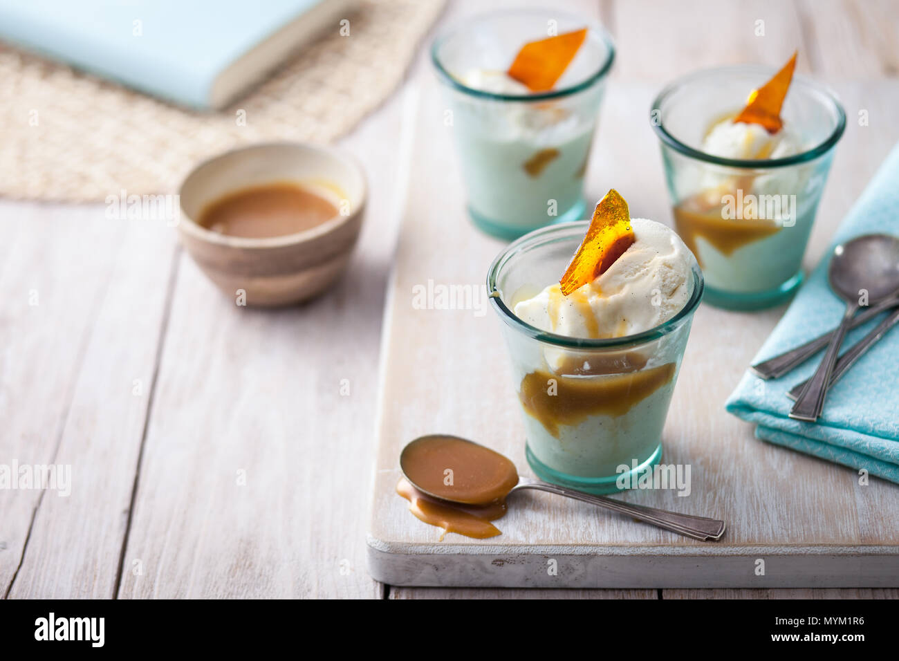 Vanille Eis im Glas serviert Gerichte mit Butterscotch Sauce und Karamell shard auf einem urigen weiß Arbeitsplatte aus Holz Stockfoto