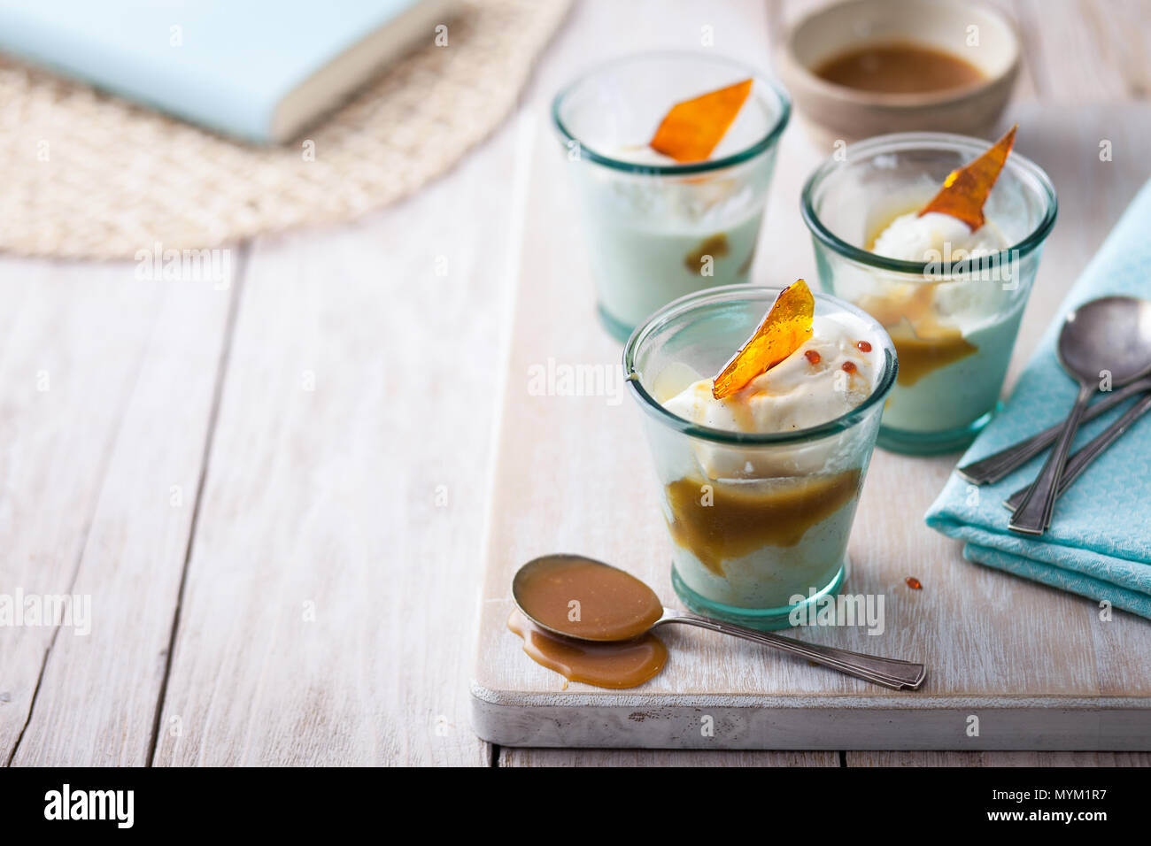 Vanille Eis im Glas serviert Gerichte mit Butterscotch Sauce und Karamell shard auf einem urigen weiß Arbeitsplatte aus Holz Stockfoto