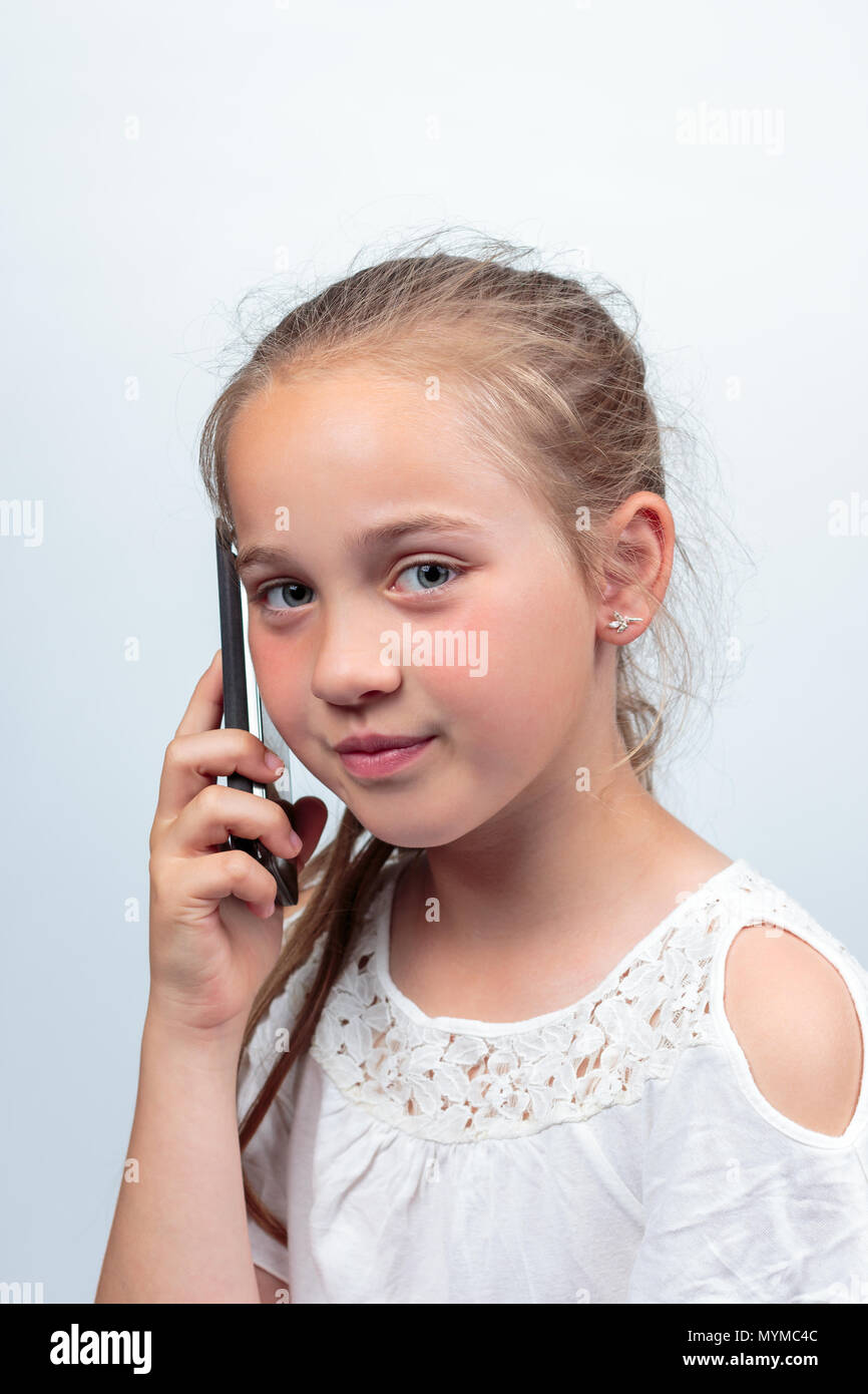 Das Porträt einer hübschen jungen kaukasischen Mädchen (10 Jahre alt) eine weiße Sommer Kleid oder Bluse Telefonieren mit einem Handy lächelte Stockfoto