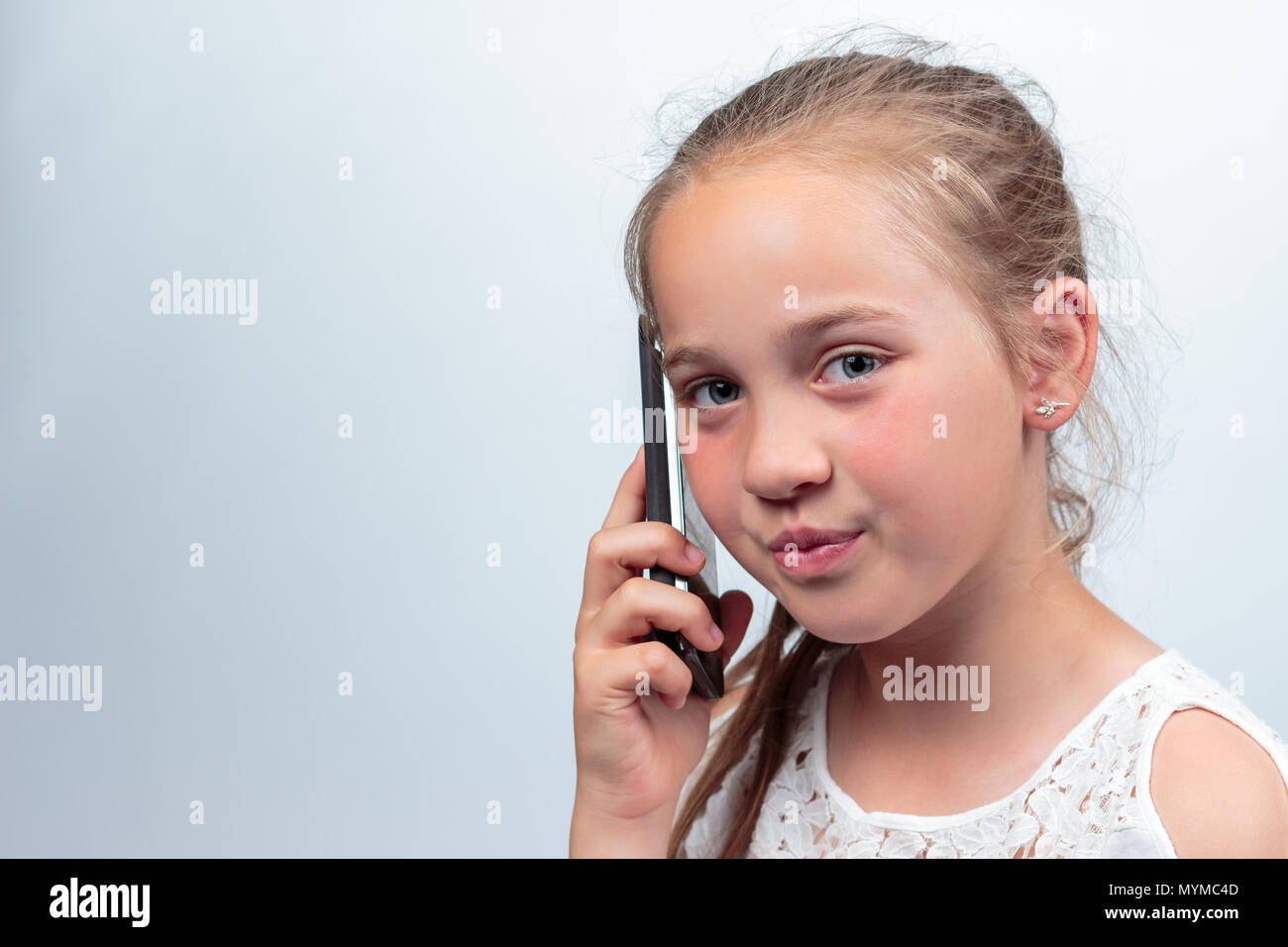Das Porträt einer hübschen jungen kaukasischen Mädchen (10 Jahre alt) eine weiße Sommer Kleid oder Bluse Telefonieren mit einem Handy ein Blick auf die Stockfoto