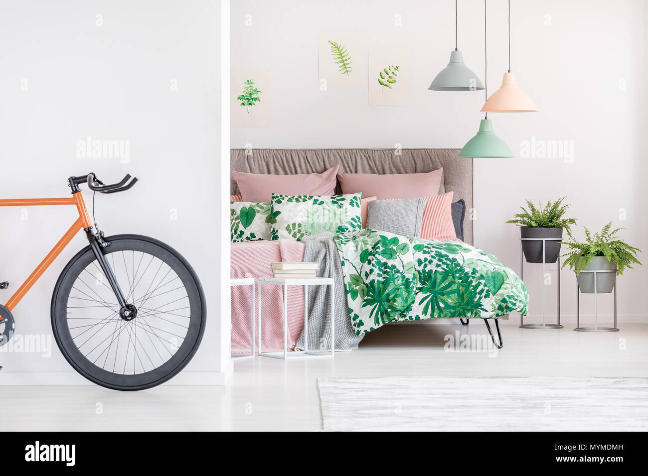 Schwarz und Orange bike stehen in Weiß Schlafzimmer mit geblümten Bettwäsche Stockfoto