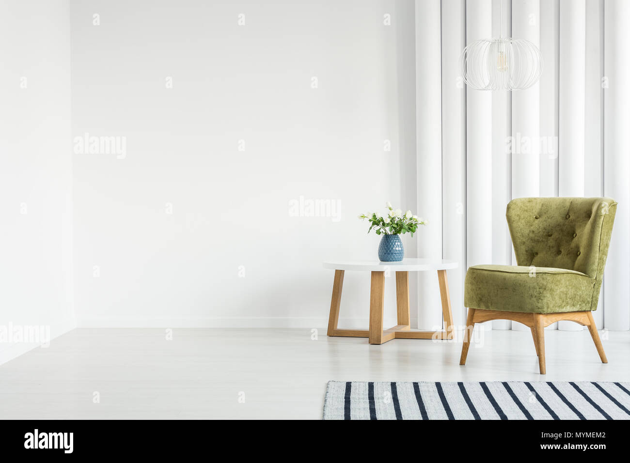 Weiß Wohnzimmer Einrichtung mit grünen Sessel neben einem Holztisch und leere Wand Stockfoto