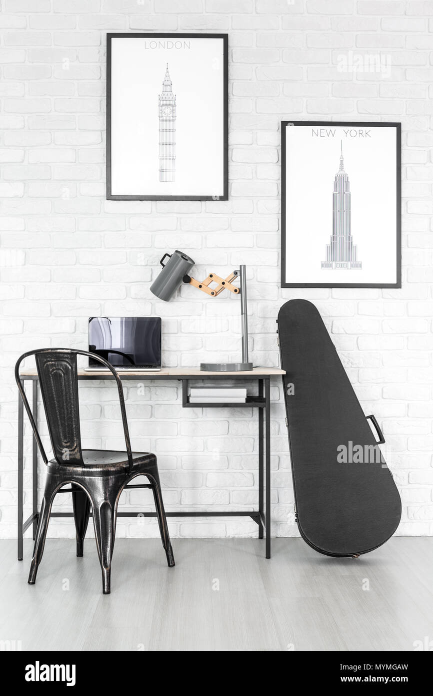 Schwarze E-Gitarre steht neben einem hölzernen Schreibtisch mit Laptop und handgefertigte Lampe im Zimmer mit Postern Stockfoto