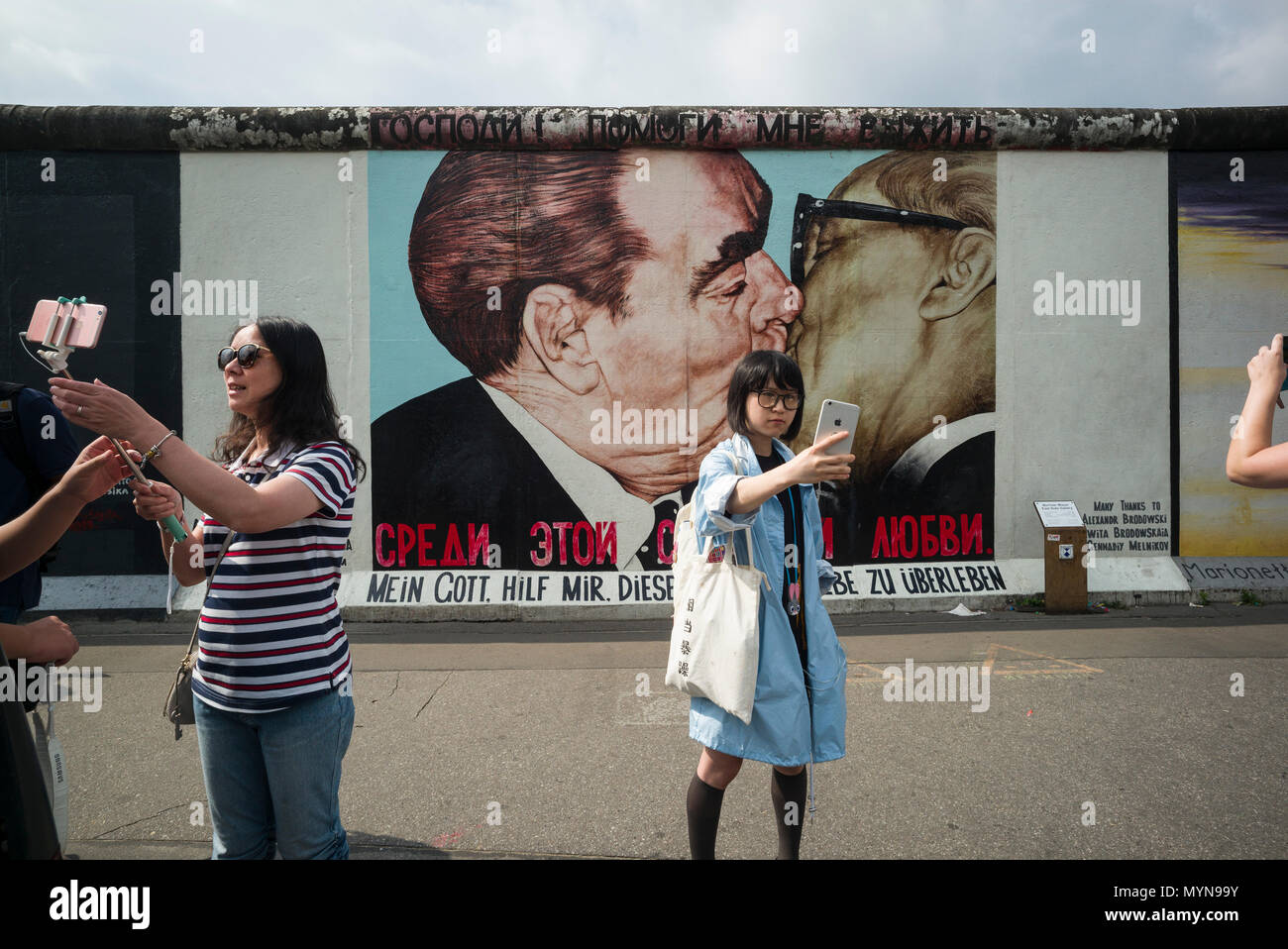 Berlin. Deutschland. Touristen posieren für Fotos vor einem der übrigen Abschnitte der Berliner Mauer an der East Side Gallery. Touristen posieren für ph Stockfoto