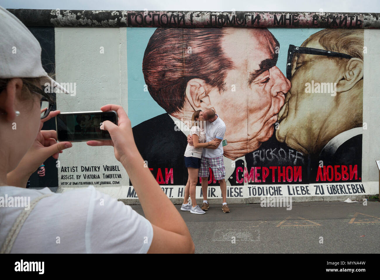 Berlin. Deutschland. Touristen posieren für Fotos vor einem der übrigen Abschnitte der Berliner Mauer an der East Side Gallery. Touristen posieren für ph Stockfoto