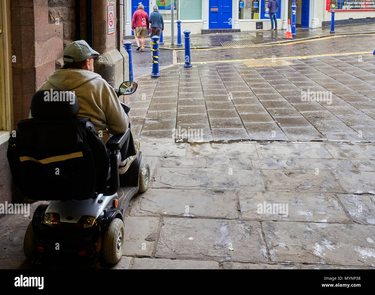 Ältere Menschen auf Mobilität scooter Unterschlupf vor dem Regen in Abergavenny, Waled Stockfoto