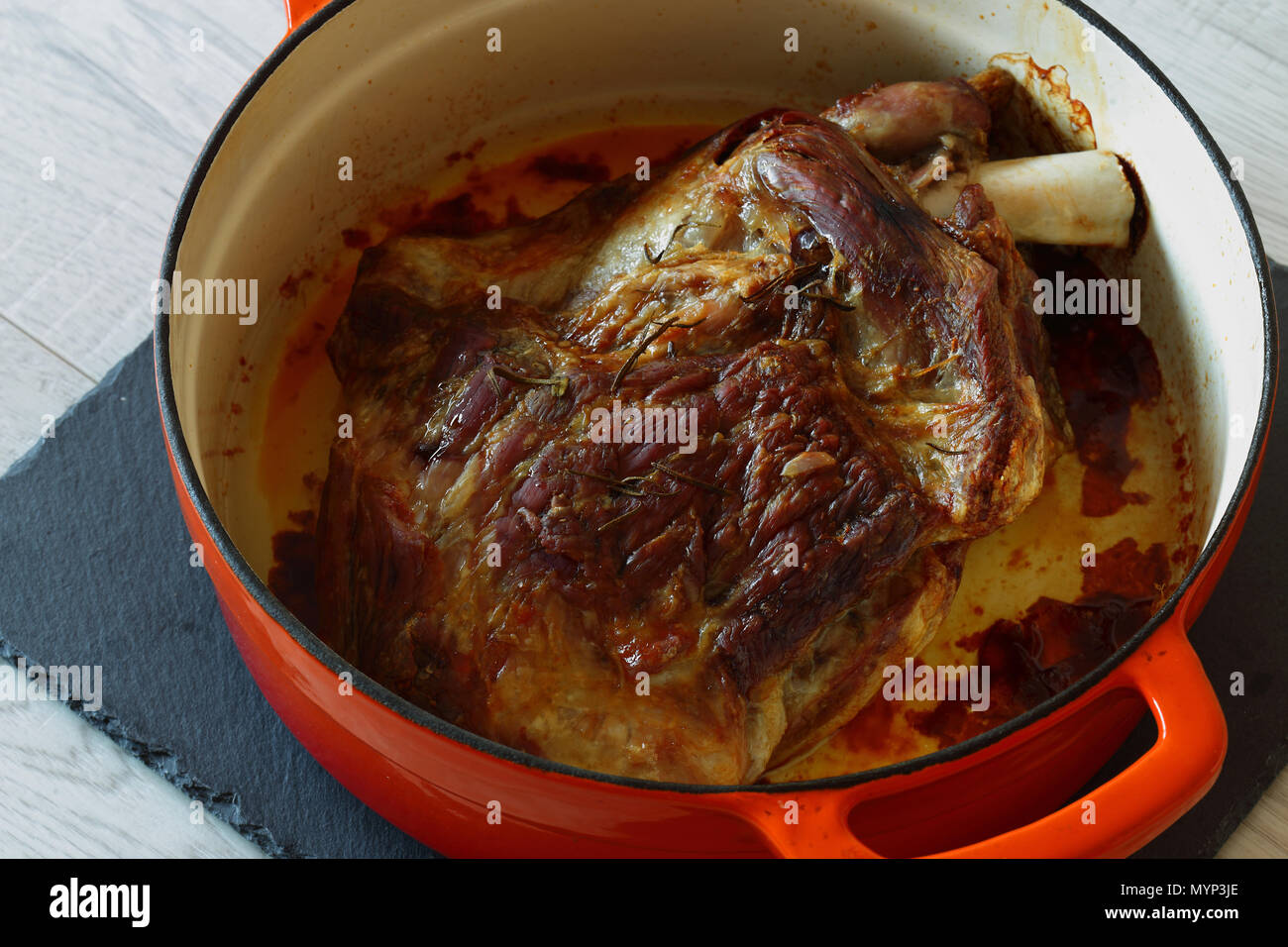 Gebratene Lammschulter in einem orange Keramik braten Teller nach dem Kochen auf Schiefer und grau Holz Küchenarbeitsplatte Stockfoto