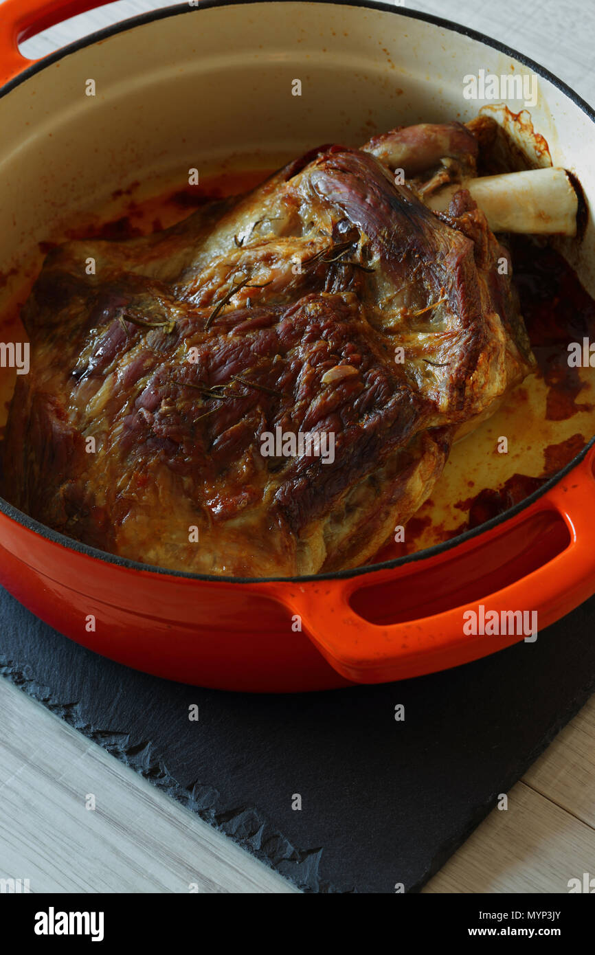 Gebratene Lammschulter in einem orange Keramik braten Teller nach dem Kochen auf Schiefer und grau Holz Küchenarbeitsplatte Stockfoto