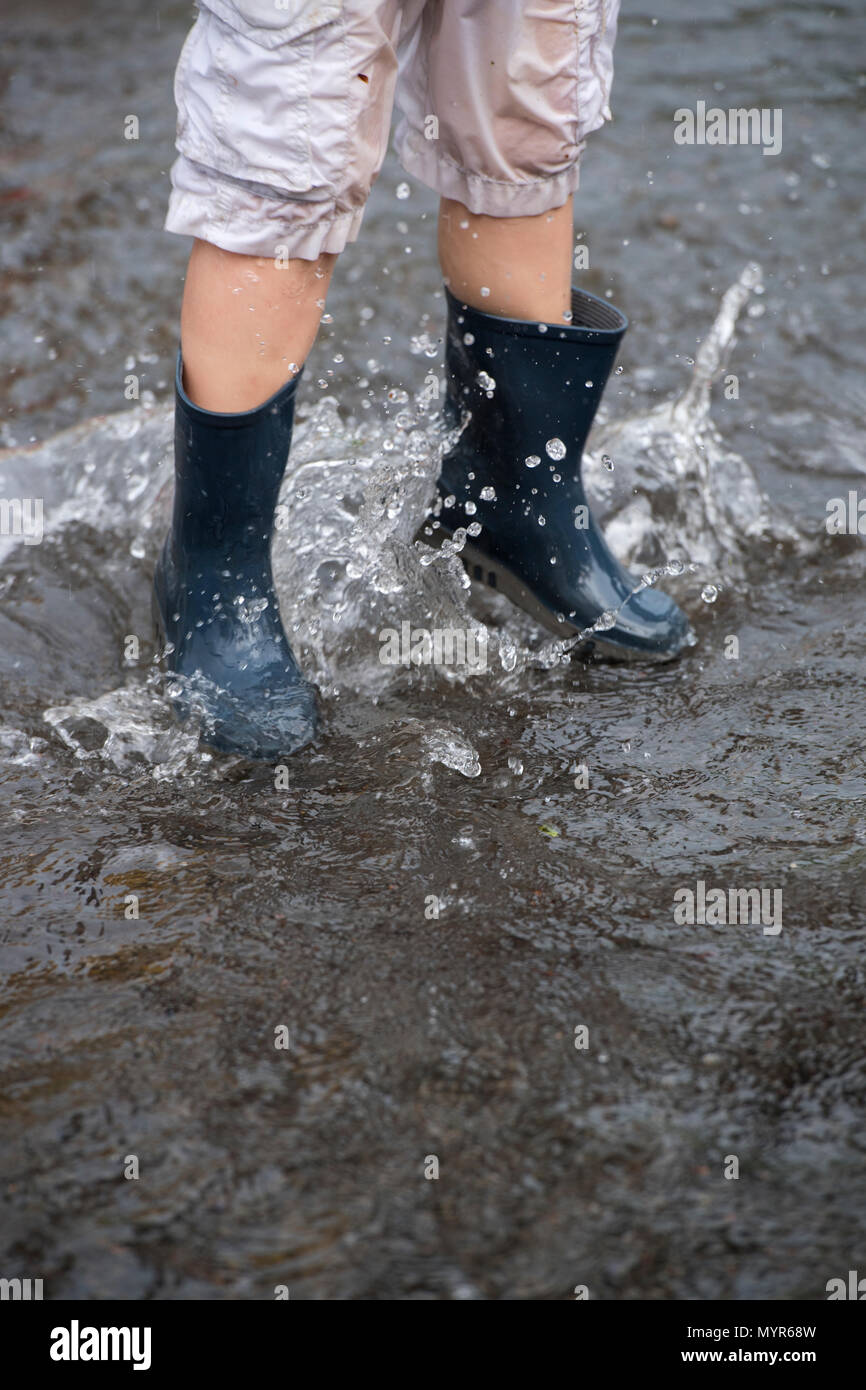 Jungen tragen Gummistiefel Spritzen in das Hochwasser in einer Straße nach schweren Regenfällen Stockfoto