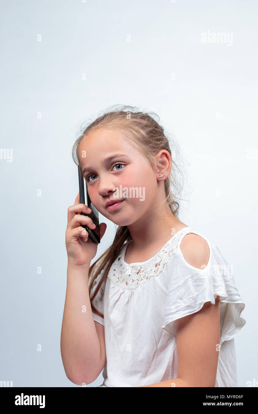 Das Porträt einer hübschen jungen kaukasischen Mädchen (10 Jahre alt) eine weiße Sommer Kleid oder Bluse Telefonieren mit einem Handy weg schauen f Stockfoto