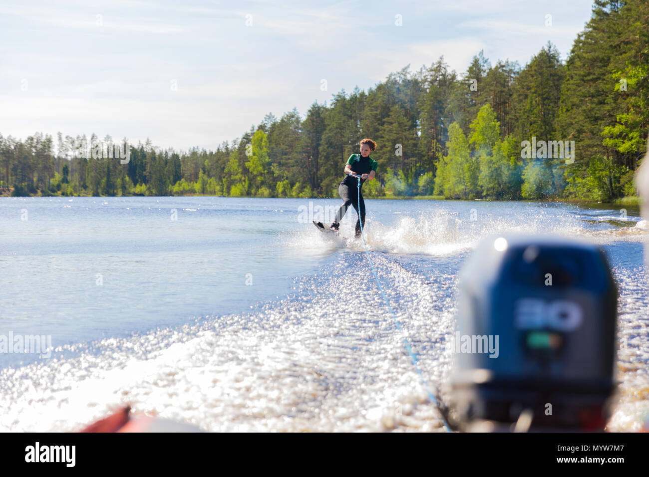 Junge hübsche schlanke Brünette Frau in Neoprenanzug reiten Wakeboard auf Welle von Motorbooten in einem Sommer See Stockfoto