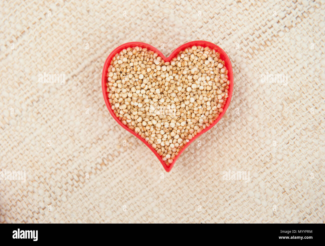 Rotes Herz mit Quinoa auf einer Leinwand Hintergrund gefüllt Stockfoto