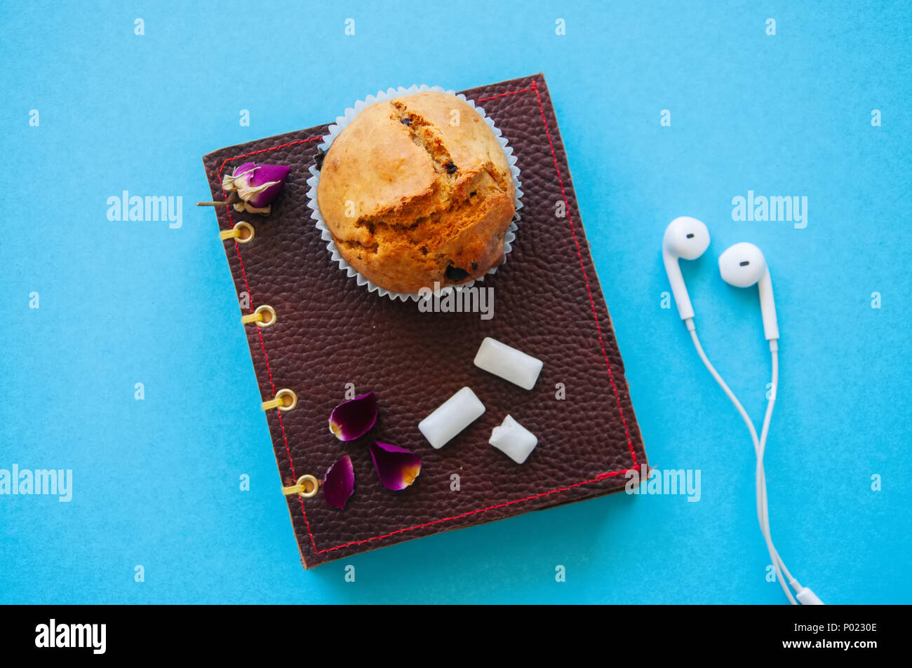 Chocolate Chip Muffins, Notebook, Ohrhörer und Kaugummis auf blauem Hintergrund, Ansicht von oben. Stockfoto