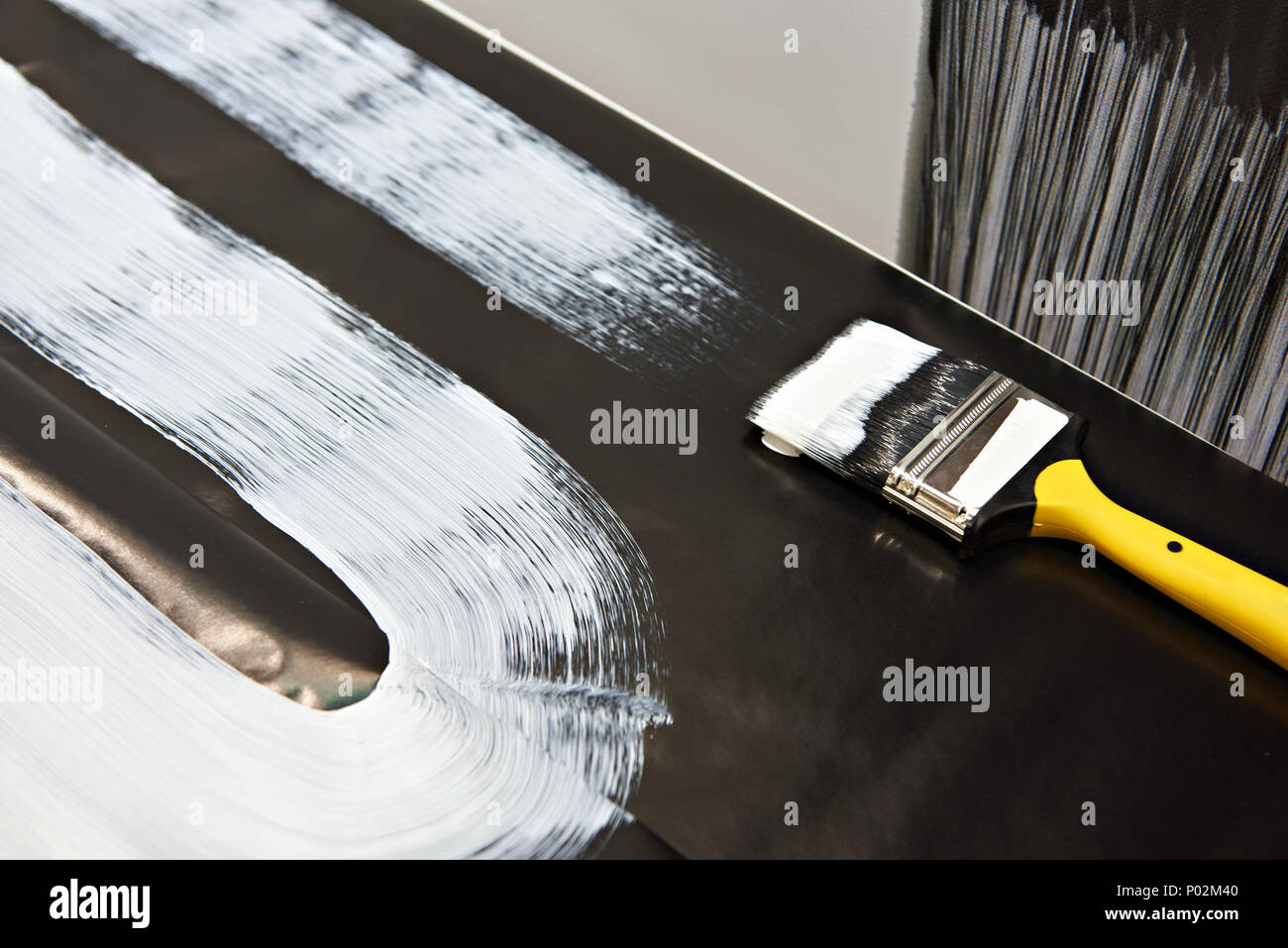 Pinsel und weiße Farbe auf eine schwarze Fläche Stockfoto