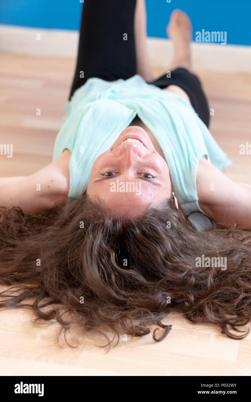 Junge Frau mit dunklen lockigen Haar ausgestreckt auf einem Holzboden und lächelnd. Von oben den Kopf gesehen. Stockfoto