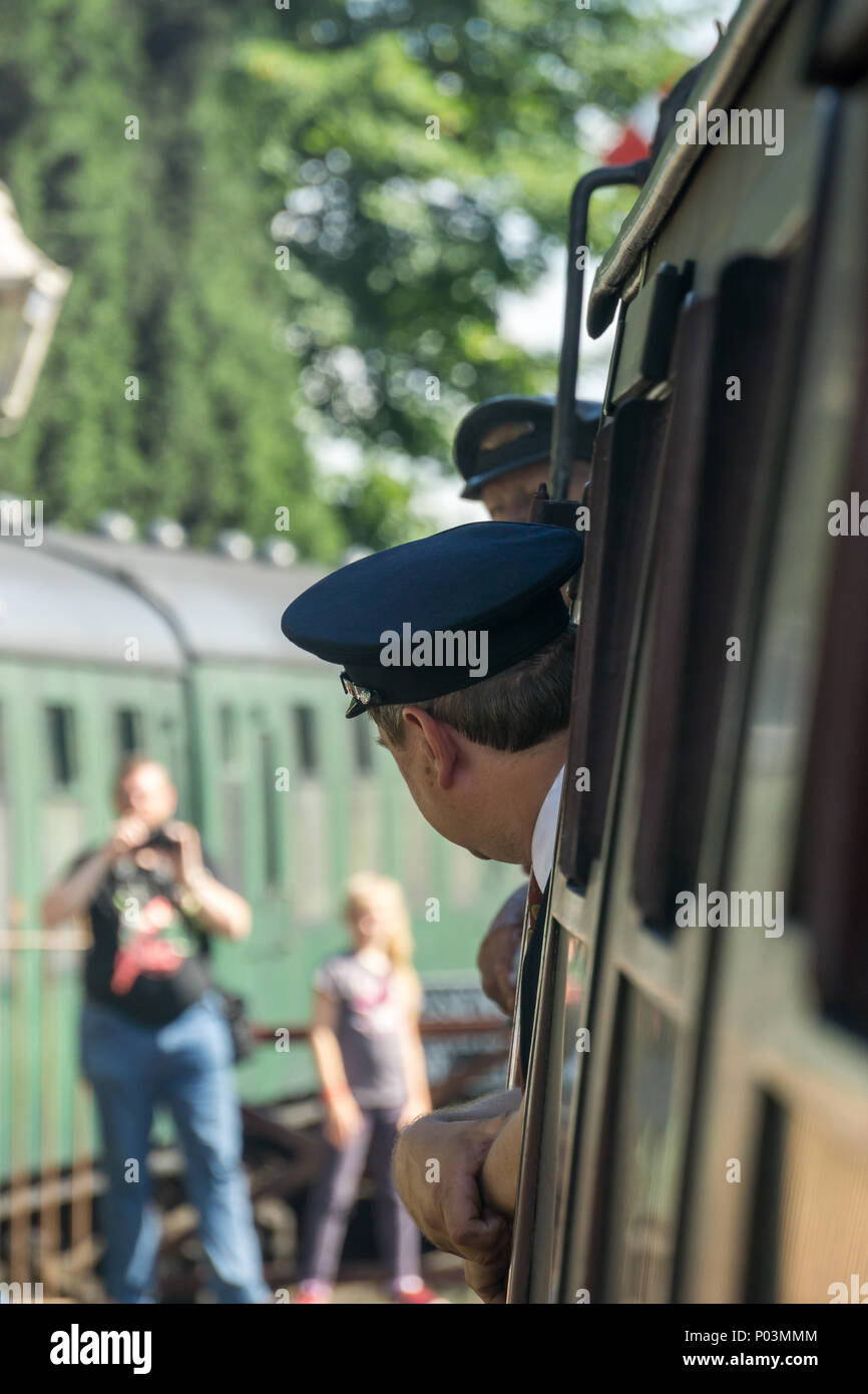 Rückansicht der Zugbegleiter (Guard) in Uniform, auf vintage UK Dampfzug, Kopf aus Fenster als Zug geht Heritage Railway Station. Stockfoto